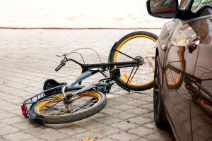 Bike laying in the street next to a car after collision. If you’ve been injured while riding a bicycle, contact a bike accident lawyer today.