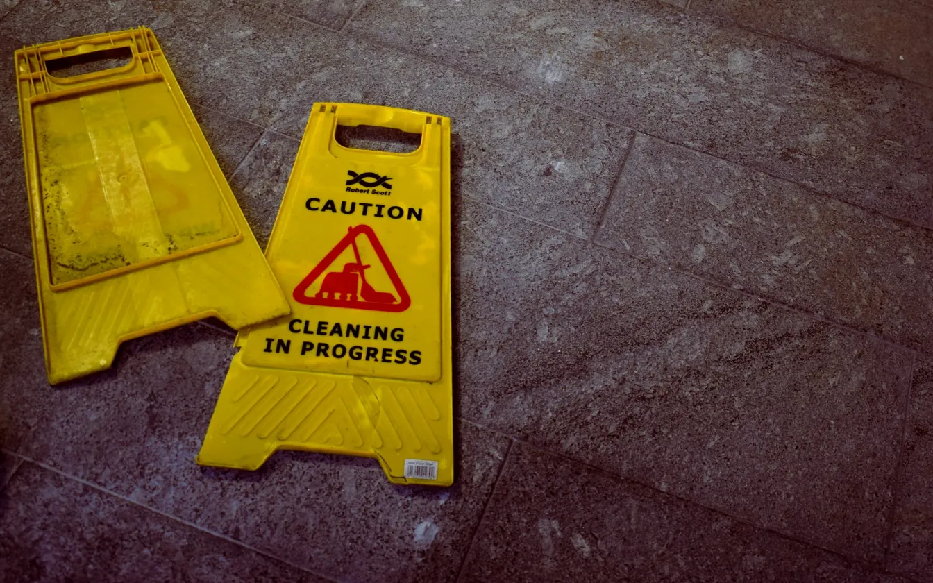 Broken wet floor caution sign laying flat on a concrete floor. Our slip and fall lawyer in Kansas City can assist you with your premises liability claim if you have been injured as a result of using a faulty staircase, slipping on a wet floor, or another hazard encountered while visiting a business or private property