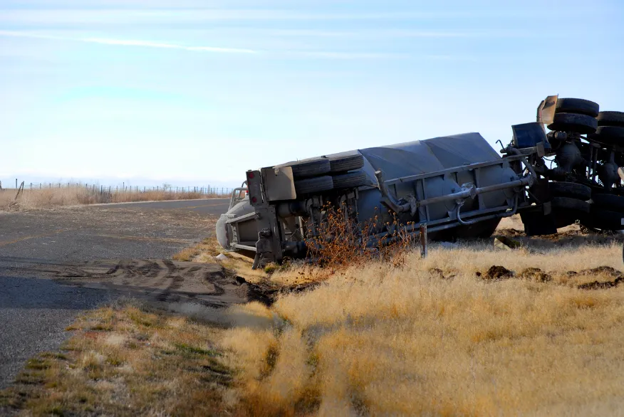 Semi truck tipped on its side in a field on the side of the road. Our highly experienced truck accident attorneys know how to fight for those injured by commercial trucks in Kansas City.