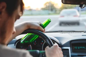 Man holding a beer and falling asleep while driving. If you’ve been injured by a drunk driver, our Kansas City drunk driving accident lawyers will fight for the justice and compensation you deserve.
