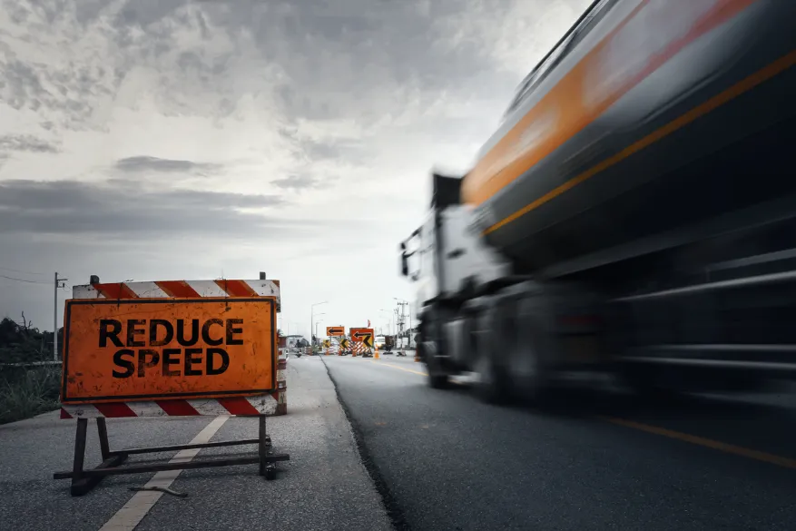 Truck speeding by a “reduce speed” sign on the freeway. If you’ve been injured due to a negligent truck driver, our Kansas City truck accident attorneys can help you.