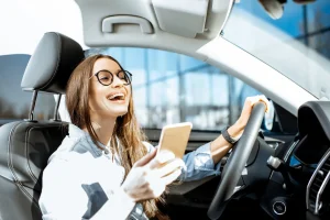 Woman driving while holding her phone and laughing. Our Kansas City texting and driving accident lawyers fight for those injured by distracted drivers.