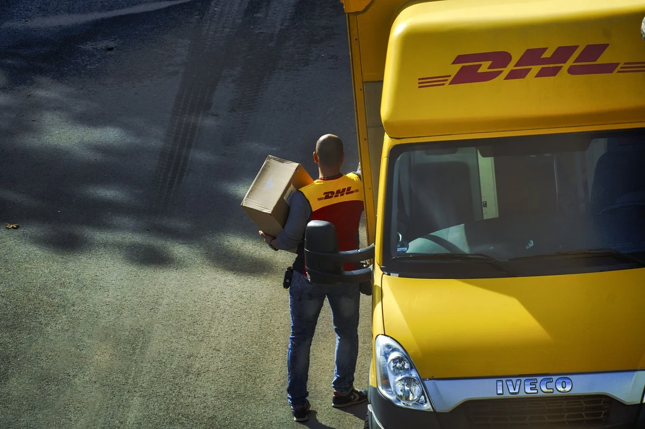 DHL truck parked with a DHL delivery driver with a package.