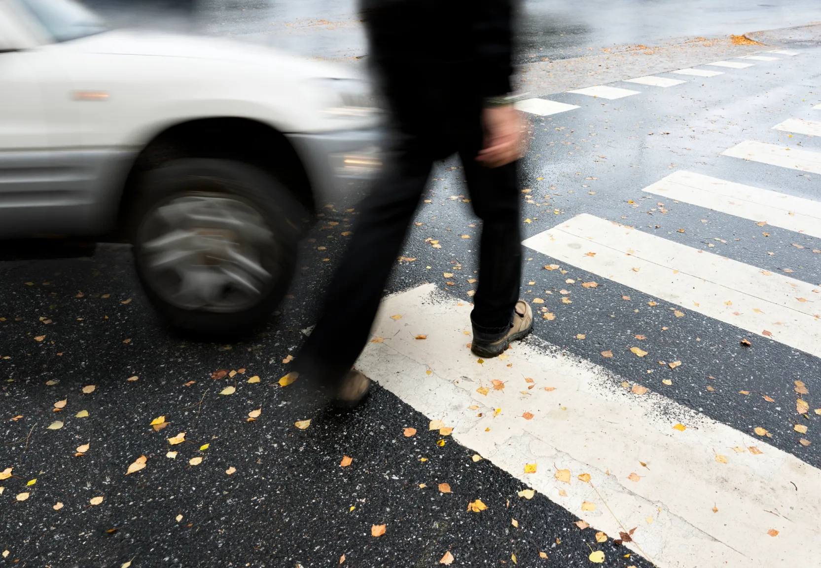 A pedestrian walking in a crosswalk with a car incoming.