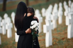 Two people hugging and crying at a graveyard. 