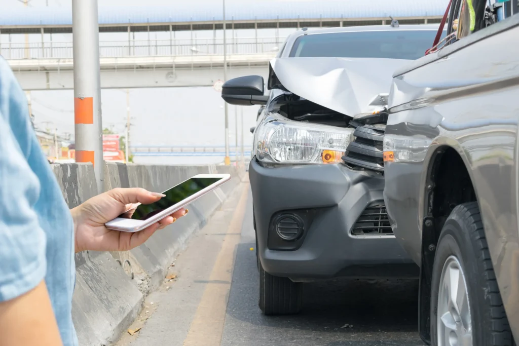 Two vehicles after an accident on the side of a highway with a woman typing on her phone.